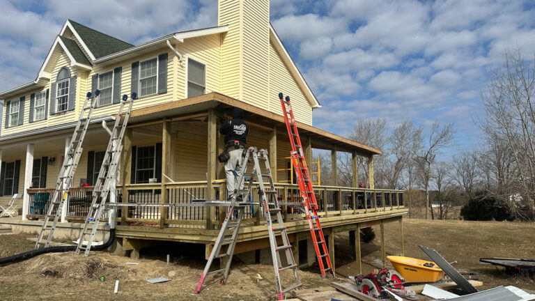 Crew rebuilding a wrap-around porch with treated lumber, ladders and safety gear